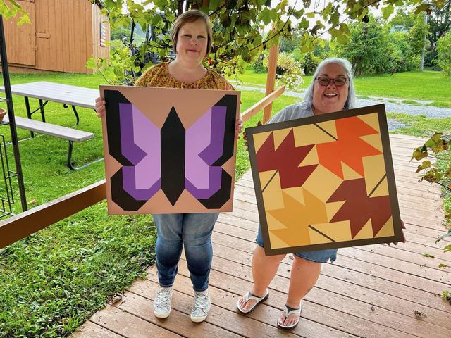 Two guests on the deck holding the barn quilt boards they painted at a workshop