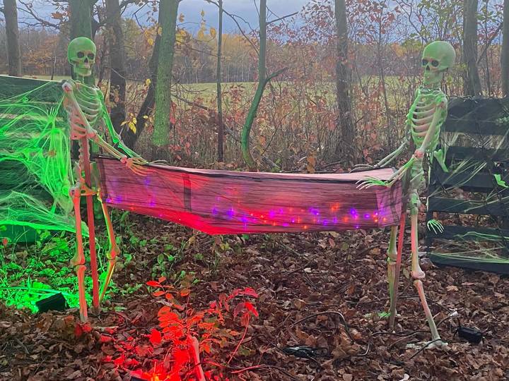 Two glowing skeletons carrying a stretcher strung with red and purple lights along the Haunted Lane