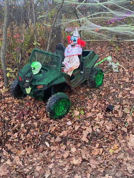A clown and a skull riding an off-road buggy in the woods, cobwebs overhead