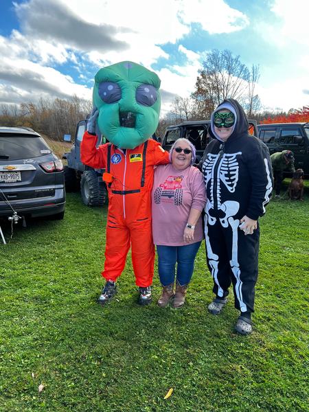 Kimm between two costumed guests at the trunk-or-treat &mdash; an inflatable alien astronaut and a skeleton onesie